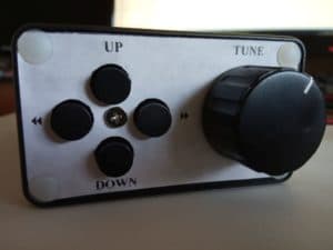 The front panel contains the tuning knob on the right side and four buttons in a cross configuration on the left
